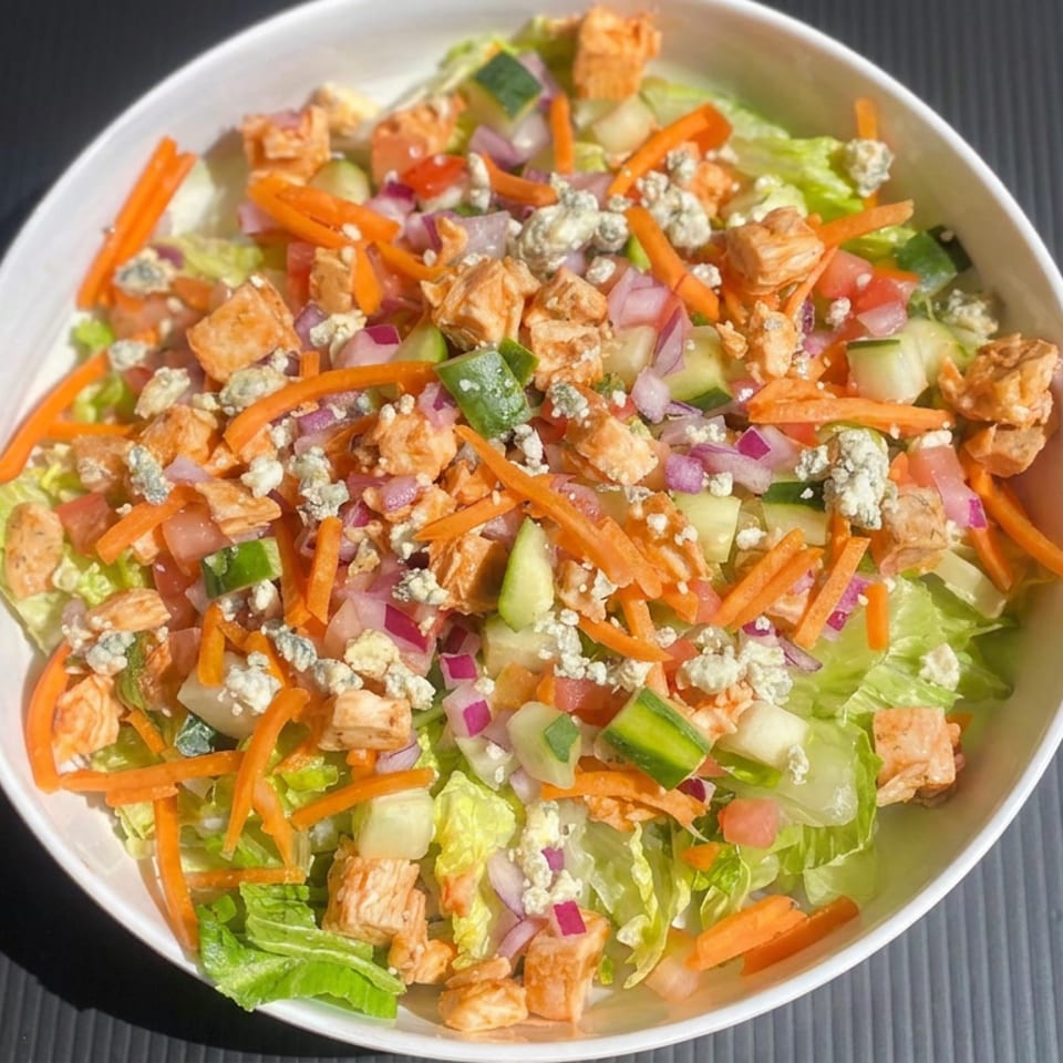 Bowl of chopped salad with lettuce, carrots, cucumbers, tomatoes, red onion, blue cheese crumbles, and grilled chicken.
