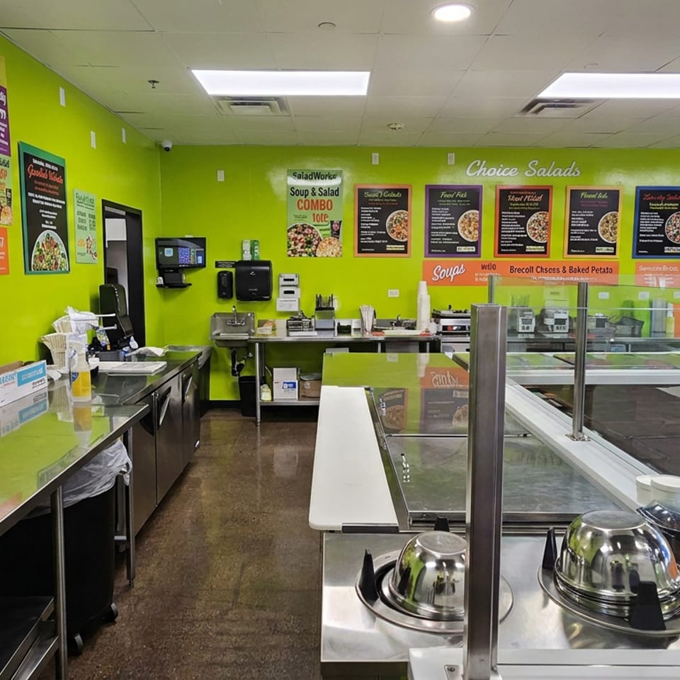 Bright Saladworks restaurant counter with salad bar, stainless-steel preparation surfaces, menu boards, and vibrant green walls.